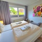 Zimmer mit Doppelbett, Fenster, Wandbild und Sitzbank.