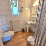 Badezimmer mit Toilette, Waschbecken und Dusche. Holzboden und Fenster mit Blick.
