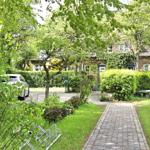 Ein gepflasterter Weg führt zu einem Haus mit Garten und Bäumen. Ein Auto steht auf dem Hof.
