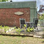 Terrasse mit Tisch und zwei Stühlen vor Backsteinwand mit Holzschild.