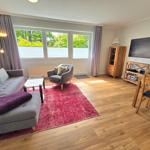 Wohnzimmer mit Sofa, Sessel, Esstisch und TV. Holzboden und großes Fenster.