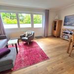 Wohnzimmer mit Sofa, Sessel, Teppich und Fenster zur grünen Aussicht.