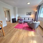 Wohnzimmer mit Sofa, Sessel, Esstisch und Holzboden. Fenster mit Jalousien.