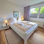 Schlafzimmer mit Doppelbett, Nachttisch und Fenster mit Blick auf Bäume.
