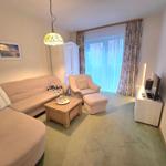 Wohnzimmer mit Sofa, Sessel, Couchtisch und TV. Fenster mit Vorhängen.