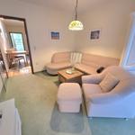 Wohnzimmer mit Sofa, Sessel und Holztisch. Durchgang zur Küche und Terrasse.