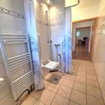 Bath with shower, seat, and grab bar. Corridor to living room.