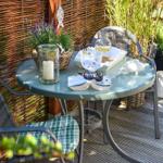 Round table with chairs on terrace, flowers and drinks on top.