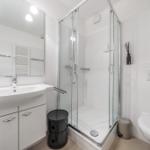 Bathroom with shower, sink, and toilet. White tiles and modern fixtures.