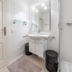 Bathroom with shower, sink, and mirror. White tiles and black trash cans.