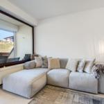 A gray sofa with cushions and a fur throw in front of a large window.