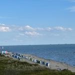 Strand mit bunten Strandkörben, Booten und Kitesurfern unter blauem Himmel.
