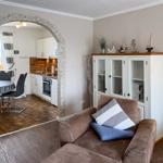 Living room with sofa and glass cabinet. Kitchen with table and chairs in the background.