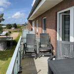 Terrace with three chairs and table, view of green area and buildings.