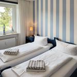 Two beds with white bedding and towels. Striped wall, window with view outside.