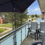 Terrace with umbrella and chairs, view of lawns and buildings.