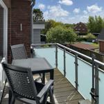 Terrace with table and chairs, glass railing, and view of garden and neighboring houses.