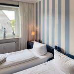 Two beds with white sheets, striped wall, and window with view of a house.