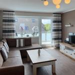 Living room with sofa, coffee table, and TV stand. Balcony with water view.