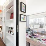 Living room with window, balcony, and floral rug. Bookcase and pictures on the wall.