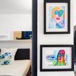 Two colorful paintings on the wall. In the background, a bed and a sofa are visible.