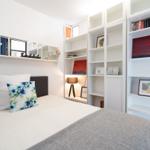 Bedroom with bed, white shelves, and window. Decorated with pictures and pillows.