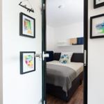 Bedroom with bed, wall art, and door. Room is well lit and modernly furnished.