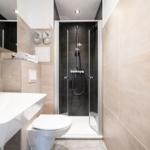 Bathroom with shower, sink, and toilet. Tiled wall and mirror visible.