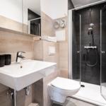 Bathroom with shower, sink, and toilet. Tiles in beige tones.