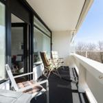 Terrace with chairs and table, view of trees. Glass facade leads into interior.