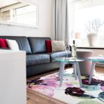 A living room with a black sofa, a colorful rug, and two glass tables.