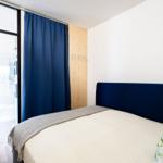 Bedroom with bed, blue headboard, and view into the kitchen.