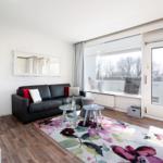 Living room with sofa, TV, and balcony door. Floral rug and large window.