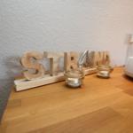 Holzdekoration mit dem Wort STRAND auf einer Holzoberfläche neben einer Waschschale.