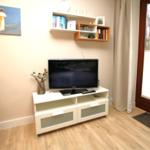 TV auf weißem Schrank, Wandregal mit Büchern, Fenster mit Jalousie und Holzboden.