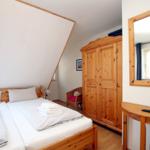 Schlafzimmer mit Doppelbett, Holzschrank und Spiegel an der Wand.