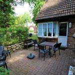Terrasse mit Tisch, Stühlen und Gartenhaus. Umgeben von Bäumen und Sträuchern.