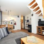 Wohn- und Küchenbereich mit Sofa, TV und Holztreppe.