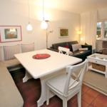 Living and dining area with white table, sofa, and window overlooking garden.