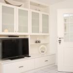 Weißer Schrank mit Fernseher und offenen Regalen. Tür mit Glasfenstern führt in einen anderen Raum.