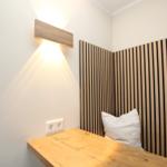 Ein kleiner Schreibtisch mit Holzplatte und Wandbeleuchtung neben einem Sitzbereich mit Holzpaneelen.