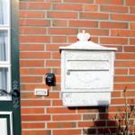 Weißer Briefkasten an roter Ziegelwand neben grüner Tür mit Fenster.