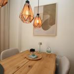 Holztisch mit Stühlen, zwei Hängelampen und Wandbild.