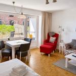 Living space with sleeping area, dining table, red armchair, and floral-patterned sofa.