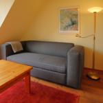 Ein Wohnzimmer mit grauem Sofa, Holztisch und Stehlampe. Wandbild und Holzfußboden sind sichtbar.