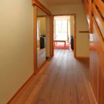 Flur mit Holzboden, Treppe und Blick in Wohnzimmer mit Sofa und Tisch.