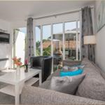 Wohnzimmer mit Sofa, Couchtisch und TV. Durchgehende Glasfront zur Terrasse.