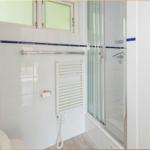 Badezimmer mit Dusche, Heizkörper und Fenster. Wandfliesen und Holzboden.