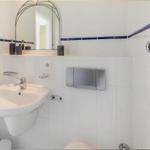 Badezimmer mit Waschbecken, Spiegel und Toilette. Weiße Fliesen mit blauer Bordüre.