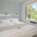 Schlafzimmer mit Doppelbett, Fenster mit Blick auf Bäume und Wand mit Tapete.